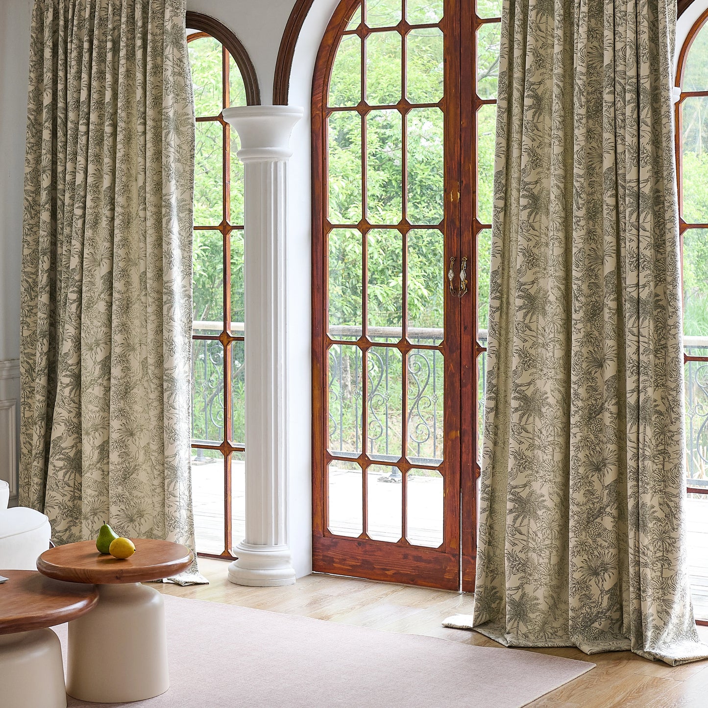 Living room with large windows featuring olive toile pattern curtains and tables.