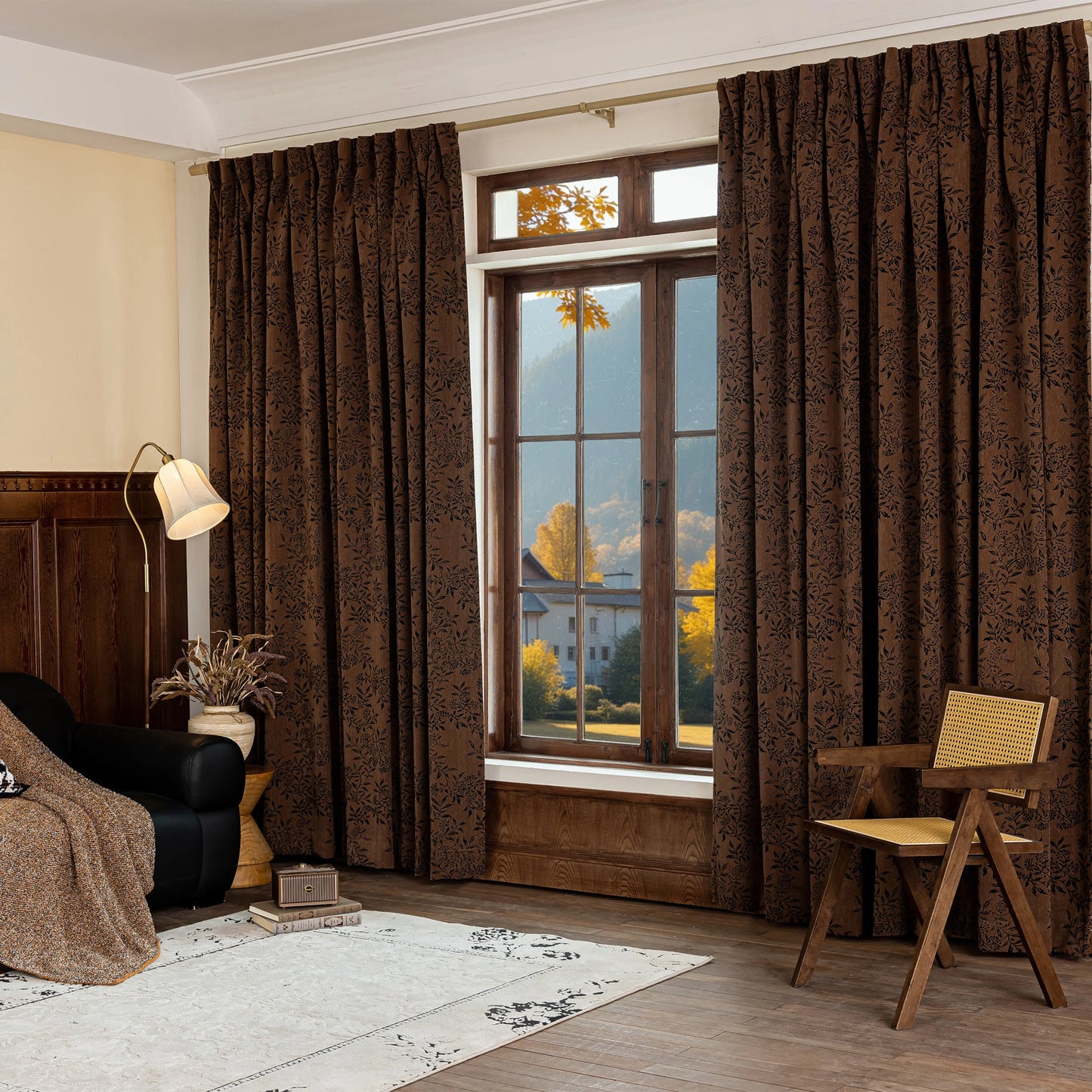 Large window with earthy-toned curtains in a dark floral pattern, accompanied by a rug, chair, and lamp.