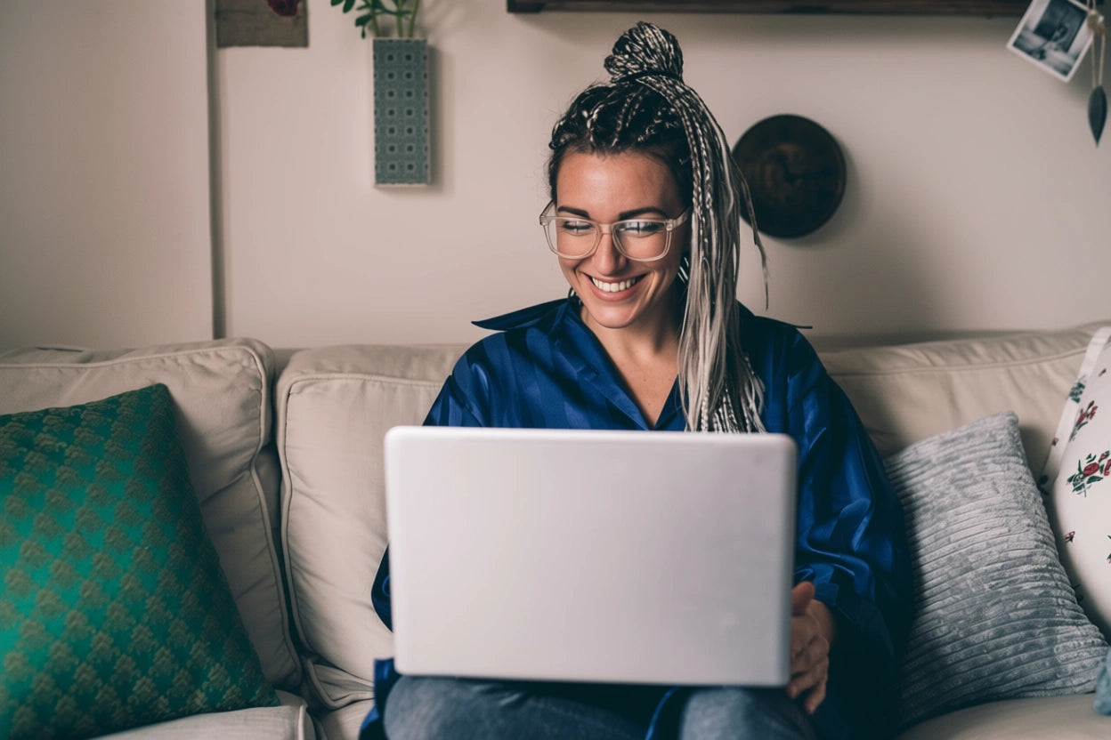 Woman sitting on a couch using a laptop, smiling.