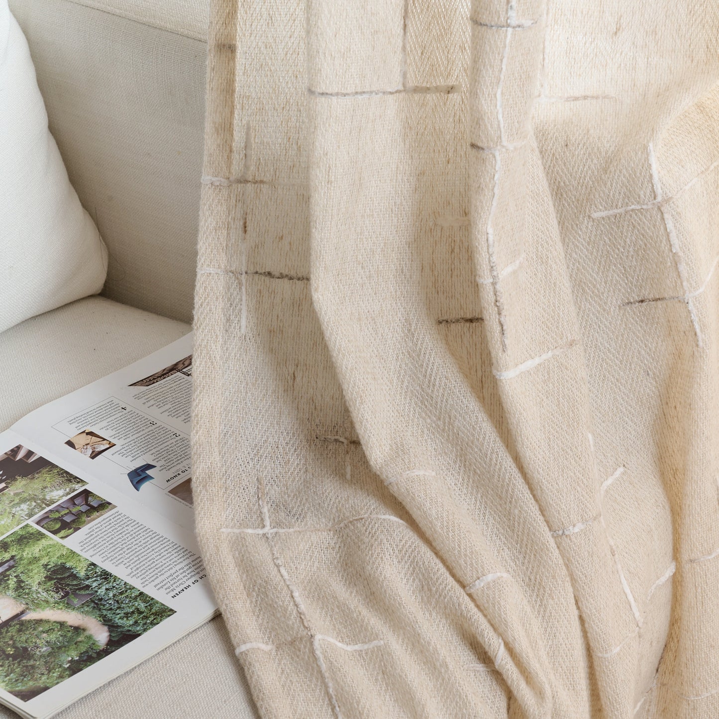 Beige wool–poly blend curtain with raised textured detailing, draped beside a light sofa, and an open magazine.
