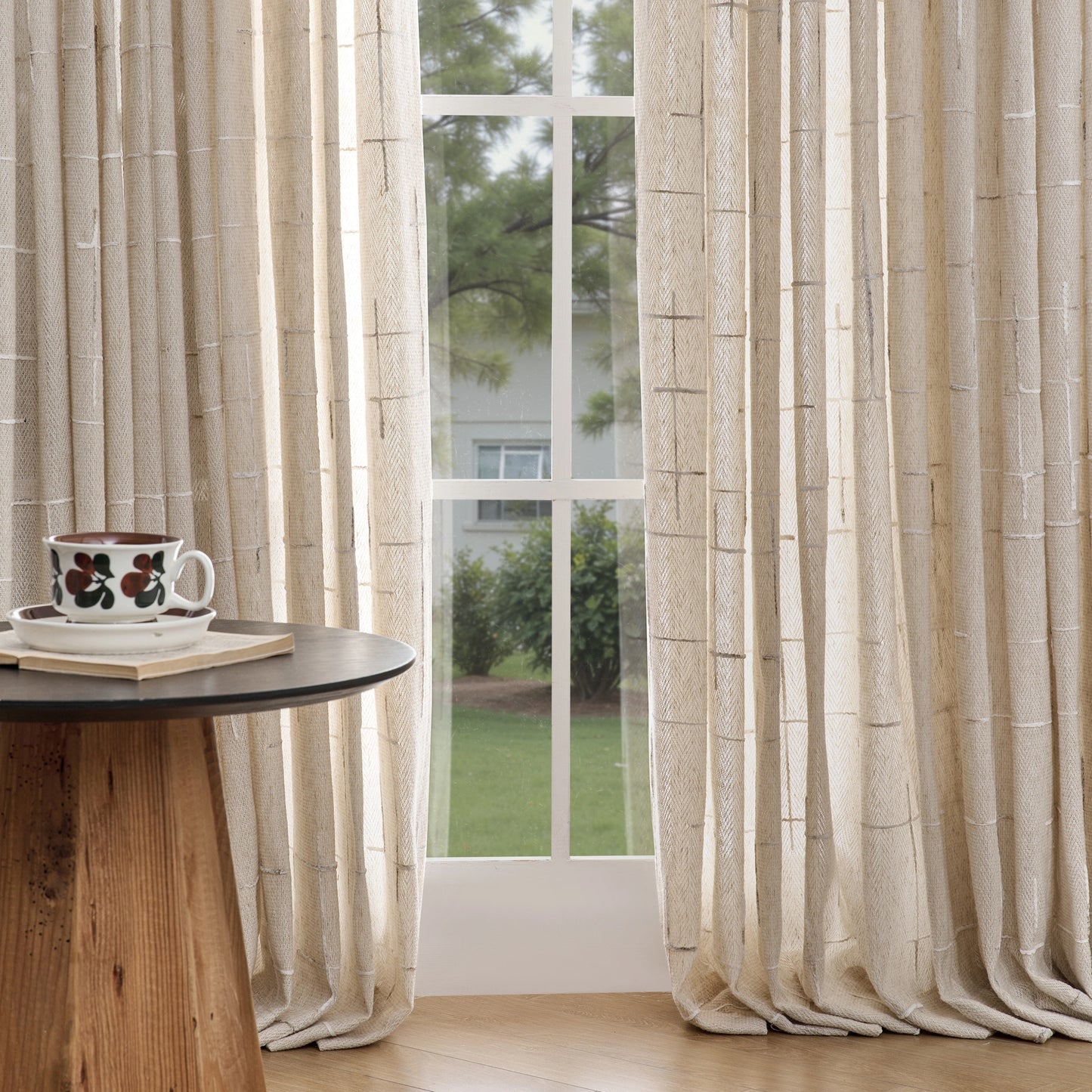 Sand curtains with raised woven detailing, set before a window, with a small round table and decorative accents.